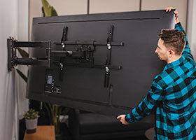 A man installing a TV on a wall using a full motion TV mount